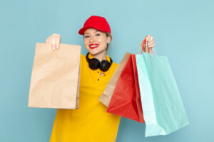 front-view-young-female-courier-yellow-shirt-red-cape-holding-multiply-shopping-packages-blue-space